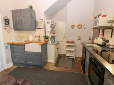 A kitchen with grey cabinets a white farmhouse sink a white door shelves with dishes and a black oven at West Wing Cottage in Hexham