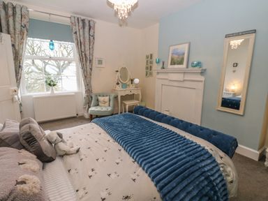 A bedroom with a bed a chair a dressing table a mirror and a window at West Wing Cottage in Hexham