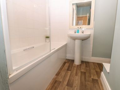A bathroom with a bathtub a pedestal sink a mirror and wooden flooring at West Wing Cottage Hexham