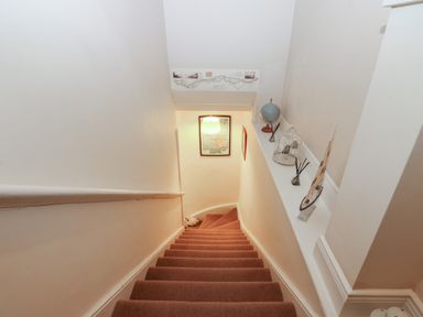 A staircase with brown carpet a handrail a globe a decorative boat and a birdcage on a shelf on the right side at West Wing Cottage in Hexham