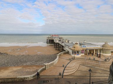 A pier extending into the sea with people walking on it and a sandy beach with pebbles at Cromer Pier