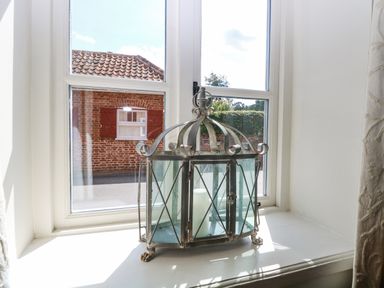 A metal and glass lantern with a candle inside on a white windowsill at Bridge Cottage in Aylsham