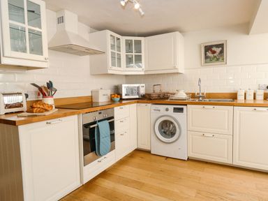 A kitchen with white cabinets wooden countertops oven washing machine and various kitchen items at Bridge Cottage in Aylsham
