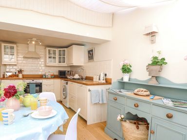 A kitchen with white cabinets wooden countertops and a blue sideboard with plants and bread at Bridge Cottage in Aylsham