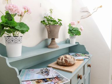 A blue wooden sideboard with potted flowers magazines and a loaf of bread on a cutting board at Bridge Cottage in Aylsham