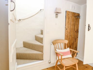 A staircase with a rope handrail next to a wooden chair with a cushion by a wooden door at Bridge Cottage in Aylsham