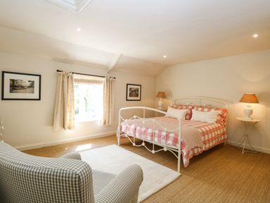 A bedroom with a white metal bed with red plaid bedding a checkered armchair and framed pictures on the wall at Bridge Cottage in Aylsham