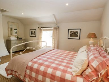 A bedroom with a white metal bed with checkered bedding a chest of drawers and framed pictures on walls at Bridge Cottage in Aylsham