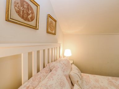 A bed with patterned pillows and a white headboard next to a nightstand with a lit lamp in a bedroom at Bridge Cottage in Aylsham