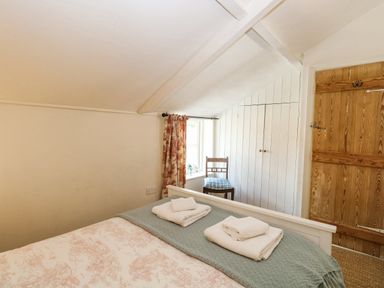 A bedroom with a bed covered with towels a chair near a window and a wooden door at Bridge Cottage in Aylsham