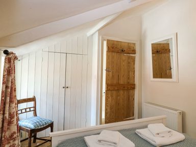 A bedroom with a bed with folded towels a wooden chair wardrobes a wooden door and a mirror at Bridge Cottage in Aylsham