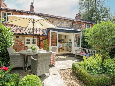 A garden patio with a table and chairs under an umbrella beside an open door to a kitchen at Bridge Cottage in Aylsham