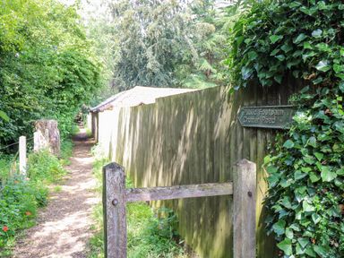A narrow public footpath with greenery and a wooden fence with a sign for Cromer Road at Bridge Cottage in Aylsham
