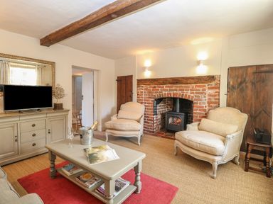 A living room with two armchairs a coffee table and a television near a brick fireplace at Bridge Cottage in Aylsham