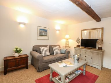 A living room with a gray sofa a coffee table and a TV cabinet at Bridge Cottage in Aylsham
