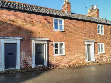 A brick exterior of a row of cottages with dark doors and white window frames at Bridge Cottage in Aylsham