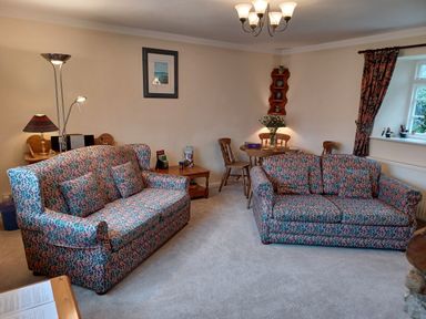 A living room with two patterned sofas a wooden dining table with chairs and a lamp at Magpie Cottage in South Brewham