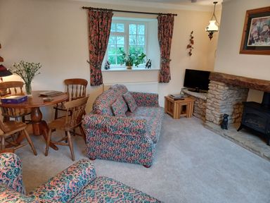 A living room with patterned sofas a wooden dining table with chairs and a stone fireplace at Magpie Cottage South Brewham
