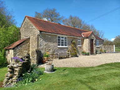 A stone cottage with a red tiled roof and potted plants on a gravel path in a grassy yard at Magpie Cottage in South Brewham