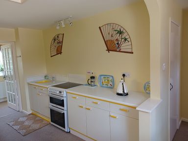 A kitchen with white cabinets yellow handles an electric stove a kettle a sink and decorative fans on the wall at Magpie Cottage in South Brewham