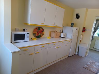 A kitchen with white cabinets yellow handles a microwave bread box toaster refrigerator and a waste bin at Magpie Cottage in South Brewham