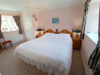 A bedroom with a large bed two bedside tables with lamps floral curtains and a window at Magpie Cottage in South Brewham