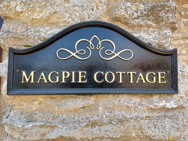 A black and gold sign reading Magpie Cottage mounted on a stone wall at Magpie Cottage South Brewham