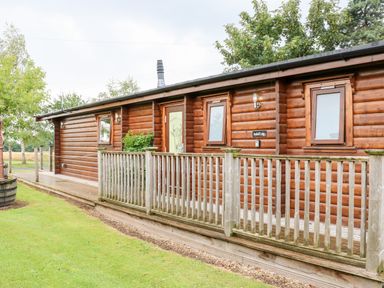 A wooden log cabin with a wooden railing and green lawn at Heathcliff in Northallerton