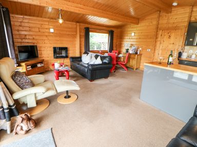 An open living room with a black sofa beige recliner red dining chairs and a television at Heathcliff in Northallerton