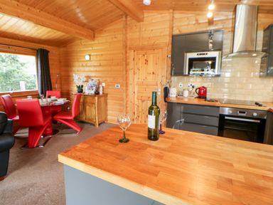 Kitchen and dining area with wooden walls red chairs and a bottle of wine on a wooden countertop at Heathcliff in Northallerton