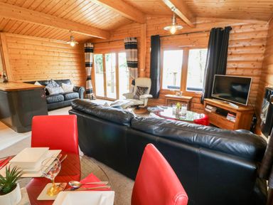A living room with black leather sofas a glass dining table with red chairs and a television at Heathcliff in Northallerton