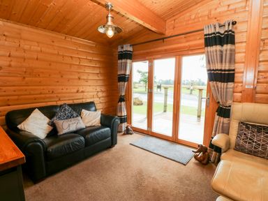 A wooden interior room with a black leather sofa and an armchair with cushions near glass doors with curtains at Heathcliff in Northallerton