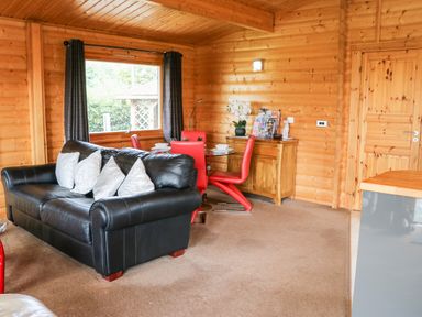 A living area with a black leather sofa and red chairs around a glass dining table in a wooden cabin at Heathcliff in Northallerton