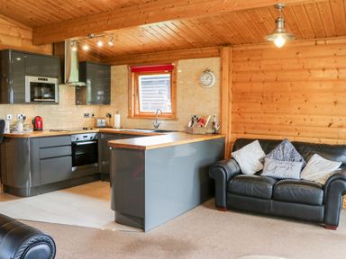A kitchen with grey cabinets and wooden countertops next to a black leather sofa with cushions at Heathcliff in Northallerton