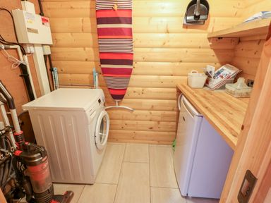 A utility room with a washing machine a vacuum cleaner an ironing board and a countertop with a small refrigerator underneath at Heathcliff in Northallerton