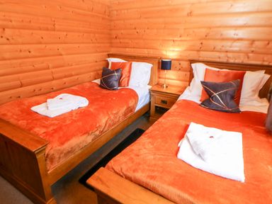 A bedroom with two single beds with orange blankets and wooden walls at Heathcliff in Northallerton