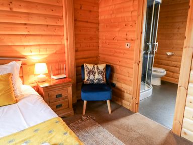 A wooden bedroom corner with a bed yellow pillow wooden nightstand lamp router blue chair with animal cushion and a bathroom visible