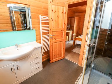 A bathroom with a white sink cabinet a turquoise backsplash a white towel radiator and a glass shower next to a wooden door leading to a bedroom at Heathcliff Northallerton