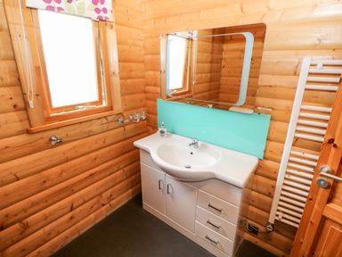 A bathroom with a white sink cabinet a rectangular mirror a window and a white towel radiator at Heathcliff in Northallerton