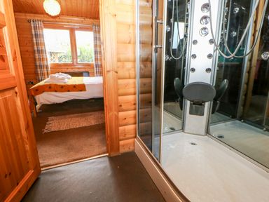 A bedroom with a bed and a window visible through a doorway from a bathroom with a shower cabin at Heathcliff in Northallerton