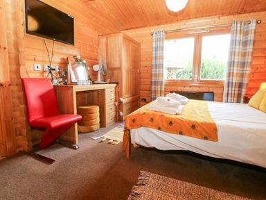 A wooden bedroom with a double bed a dressing table a red chair and a window with checked curtains at Heathcliff in Northallerton