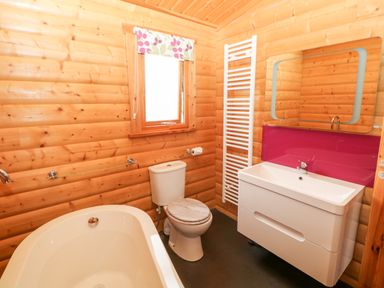 A bathroom with wooden walls a bathtub a toilet a sink with a mirror and a window at Heathcliff in Northallerton
