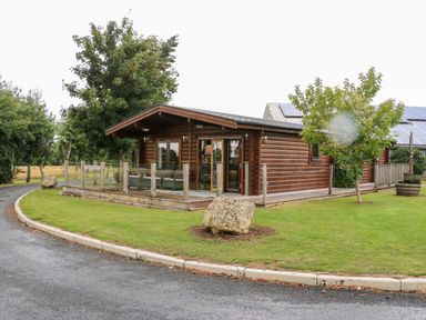 A wooden cabin with a glass fenced porch on a grassy area near a curved paved driveway at Heathcliff in Northallerton