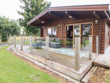 A wooden house with a glass railing porch and outdoor chairs on a grassy lawn at Heathcliff in Northallerton
