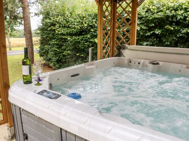 An outdoor hot tub with a bottle of wine and two wine glasses near greenery at Heathcliff in Northallerton