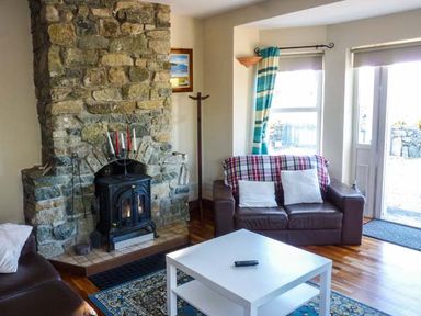 A living room with a stone fireplace a brown leather sofa a white coffee table and windows with blue curtains at Ti Sheamuis in Cashel near Carna County Galway