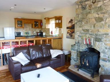 A living area with a brown leather sofa a white table a stone fireplace and a wooden kitchen at Ti Sheamuis in Cashel near Carna County Galway