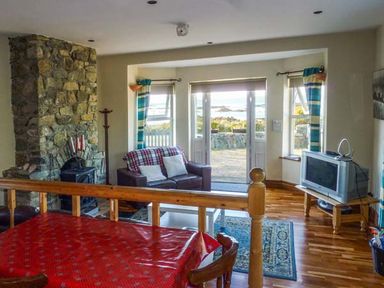 A living room with a stone fireplace a sofa and a television near windows and doors at Ti Sheamuis in Cashel near Carna County Galway