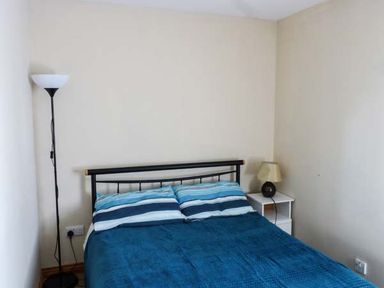 A bedroom with a double bed with blue striped pillows and blanket a floor lamp and a bedside table with a lamp at Ti Sheamuis in Cashel near Carna County Galway