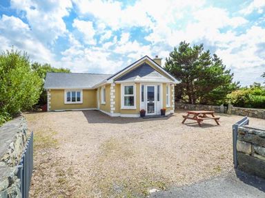 A single-story house with a gravel driveway a wooden picnic table and stone walls at Ti Sheamuis Cashel near Carna County Galway